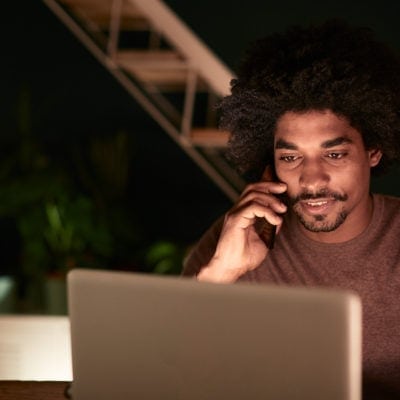 A user on the phone in from on his laptop at night at home in the dark