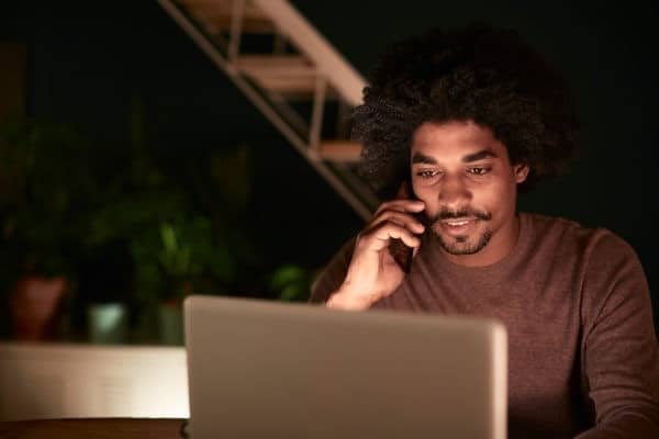 A user on the phone in from on his laptop at night at home in the dark