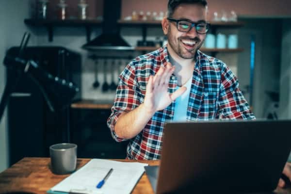 Man working from home waves at his laptop camera