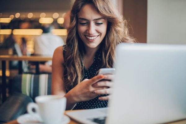 Attractive woman checks her phone in front of her laptop at a cafe