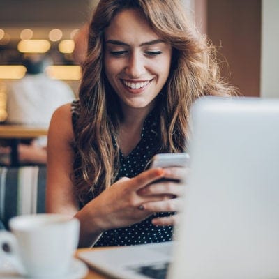 Attractive woman checks her phone in front of her laptop at a cafe